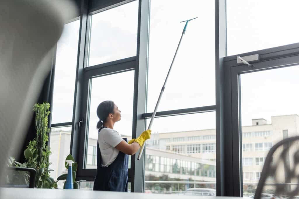 bi racial woman in workwear washing large office windows on blurred foreground