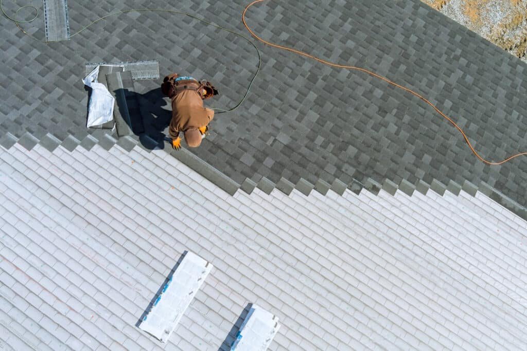 a worker installing shingles on the roof of a home with air hammer and nails
