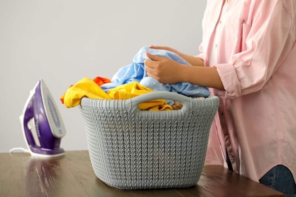 woman with basket full of clean laundry at wooden table indoors, closeup